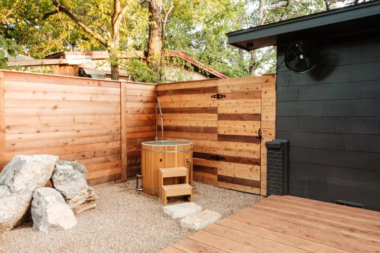 Wood outdoor soaking tub and shower beside a deck and privacy fence