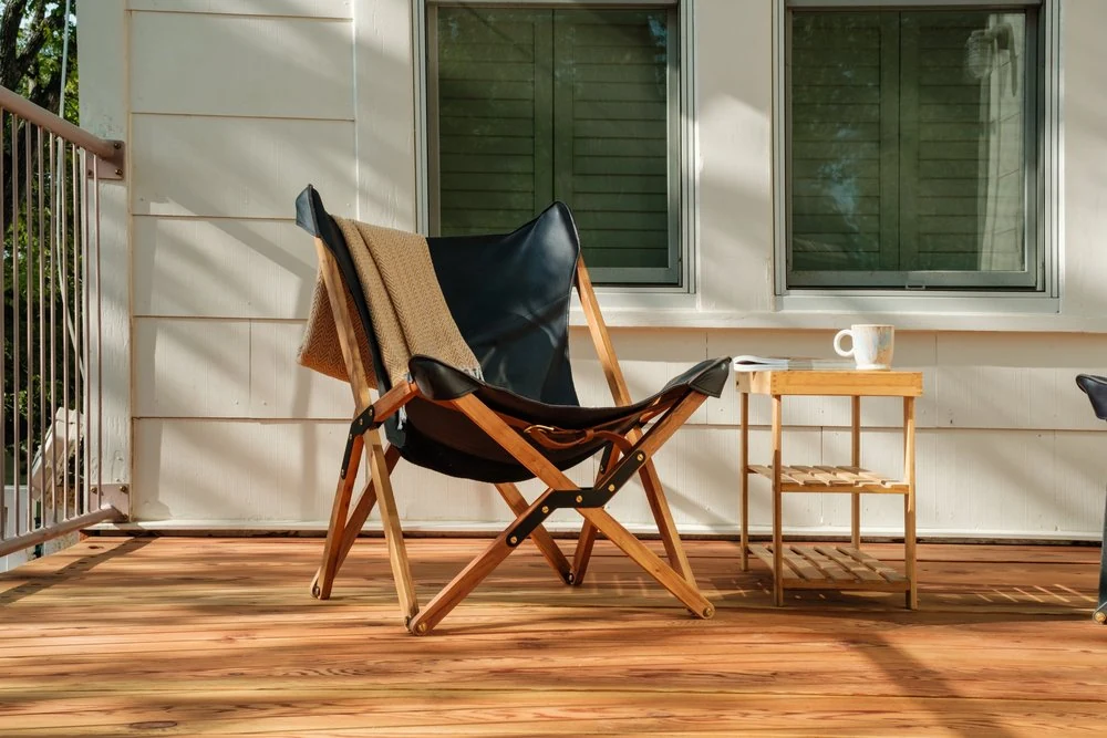 A lounge chair and coffee table on a sunny wood deck beside the home