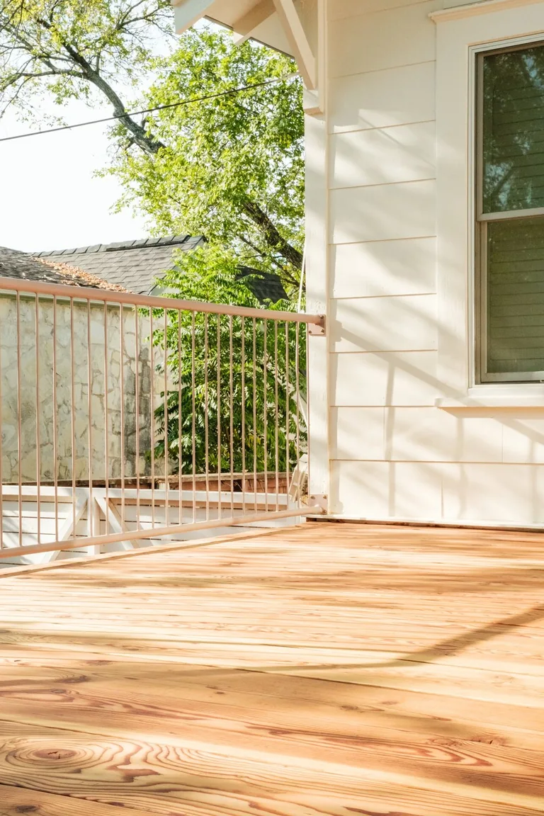 Timber deck boards meeting a white-sided home, with a railing along the open edge