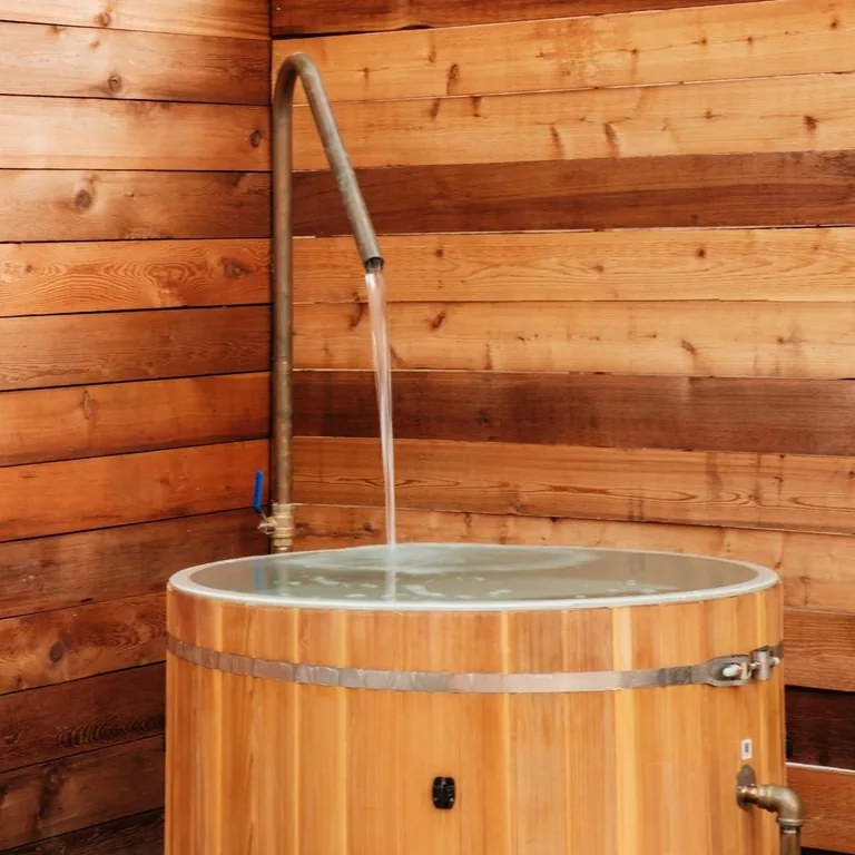 Curved outdoor shower running into a wood-sided tub between timber privacy walls