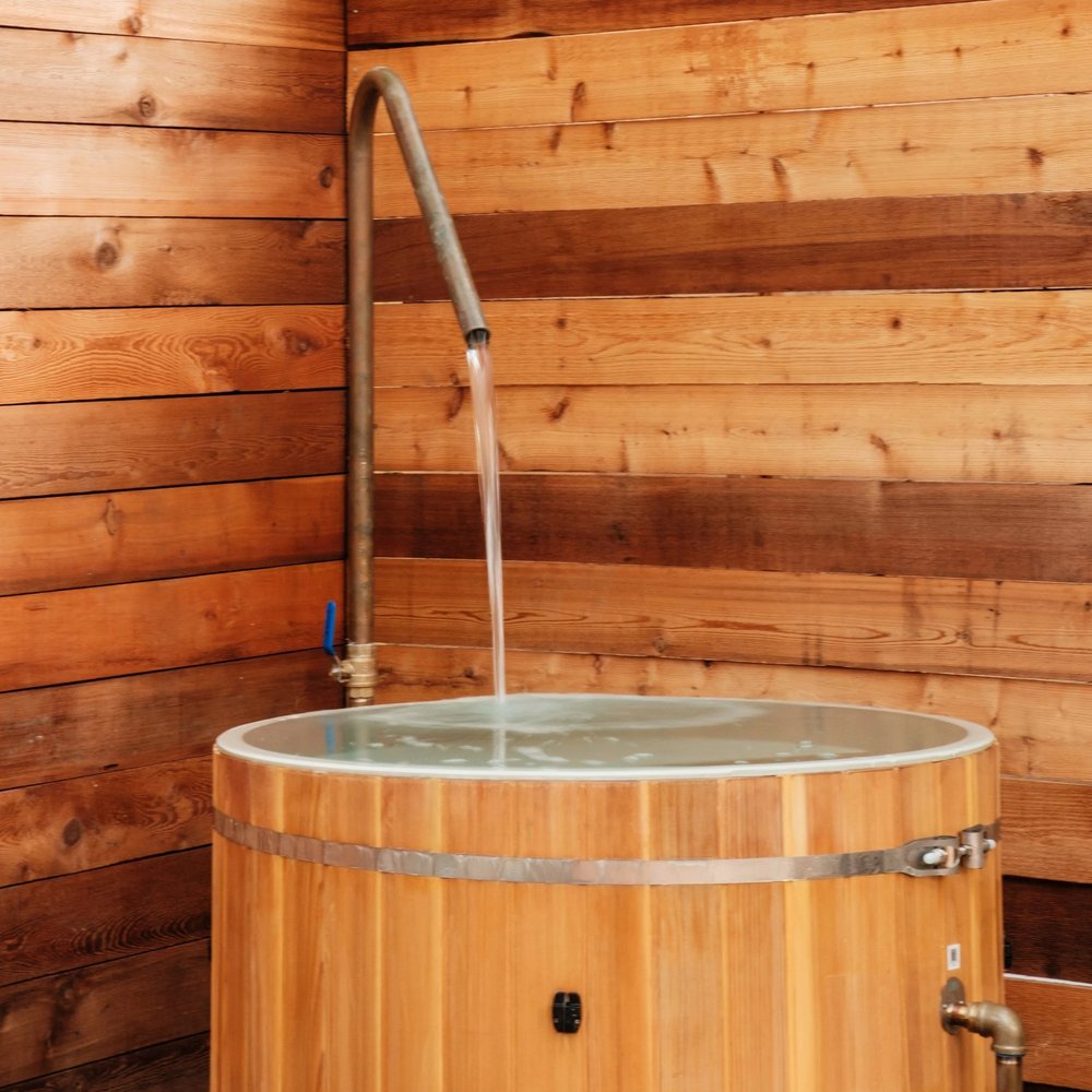 Water running from a curved outdoor shower into a wood-sided soaking tub against timber privacy walls