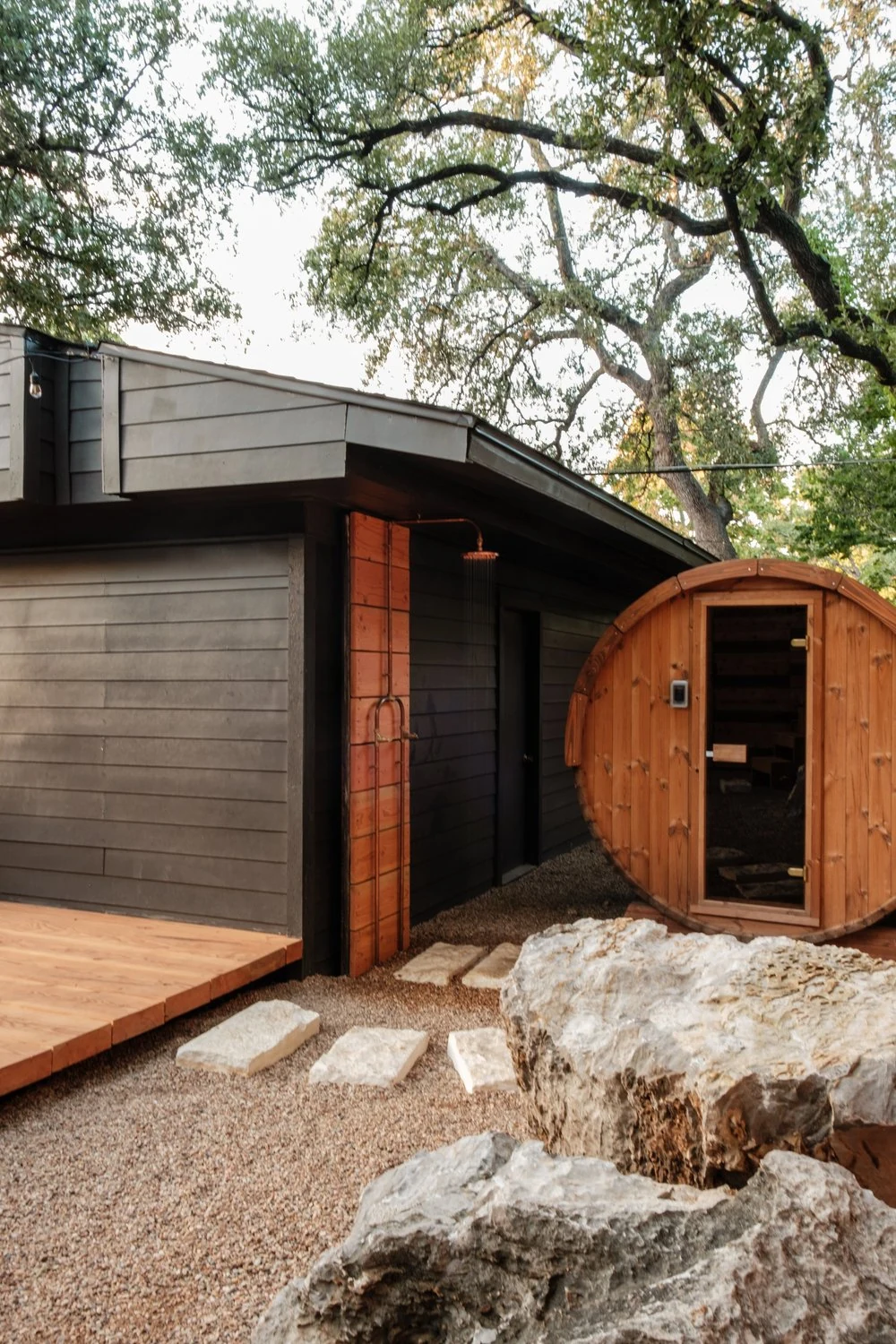 Barrel sauna beside a wood deck, stone landscape and dark garden building