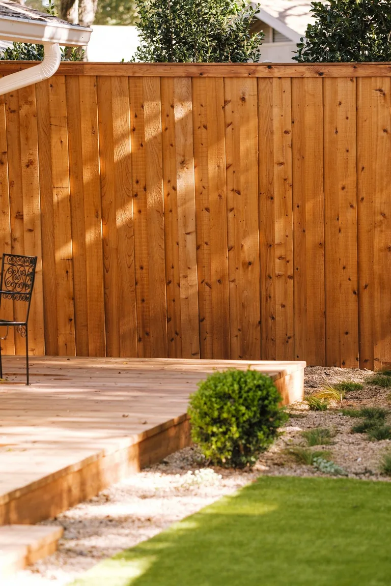 Low timber deck step beside gravel, small plants and green yard, with a timber fence behind it