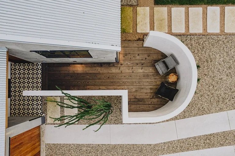 Overhead view of a curved seating wall surrounding a wood deck with planting and pale garden paths