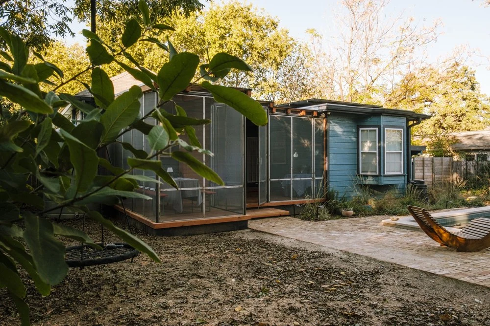 A screened porch and gravel backyard beneath mature trees